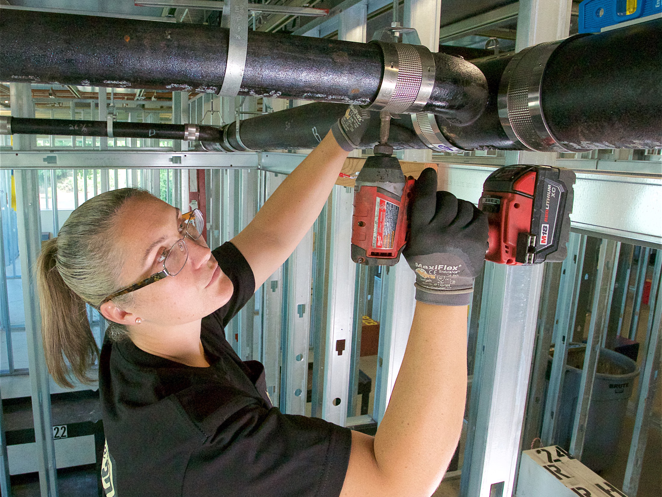 Woman tightening a pipe's fitting with a drill