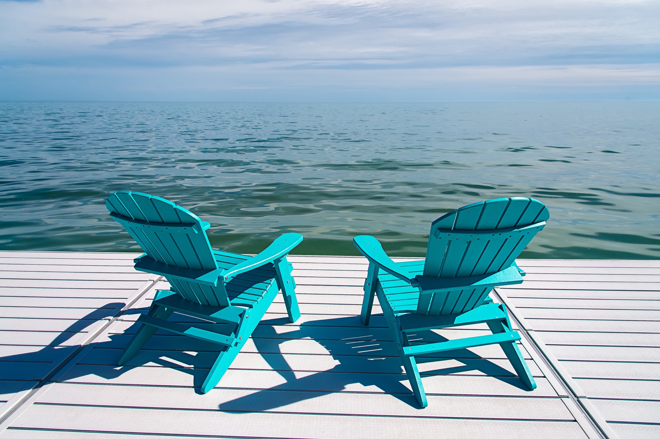 Two blue beach chairs sitting on a dock in front of open ocean